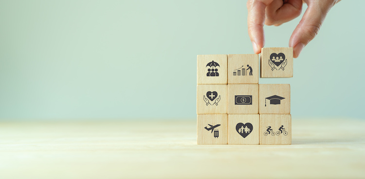Pinched fingers hold a block with a heart and people in it, placing it on the top right corner of a stack of 3 by 3 blocks each representing an employee benefit.