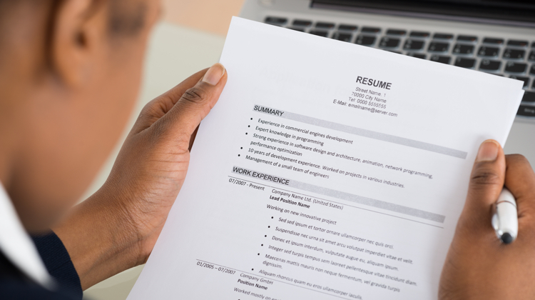 Hands hold a printed resume in front of laptop keys.