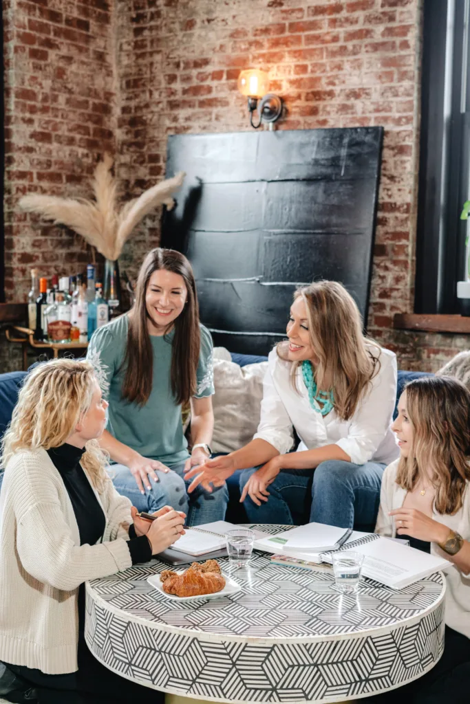 Members of the Filthy Rich Writer team sit on a couch around a table collaborating on a project with a Comprehensive Copywriting Academy workbook.