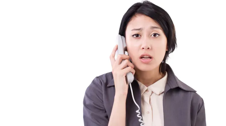 Woman holds up phone on cord to her ear with a look of dismay on face; don't make this sales call mistake if you want to land copywriting clients