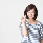 Asian woman stands against a white background in a blue and white thin striped t-shirt holds up her hand with her thumb and pointer fingers spread about one inch apart.