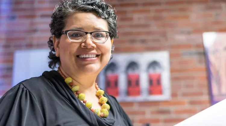 Smiling woman wearing glasses and chunky yellow necklace and black dress shirt