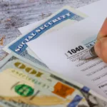 One hundred dollar bill lies on table next to tax form 1040 and a Social Security card