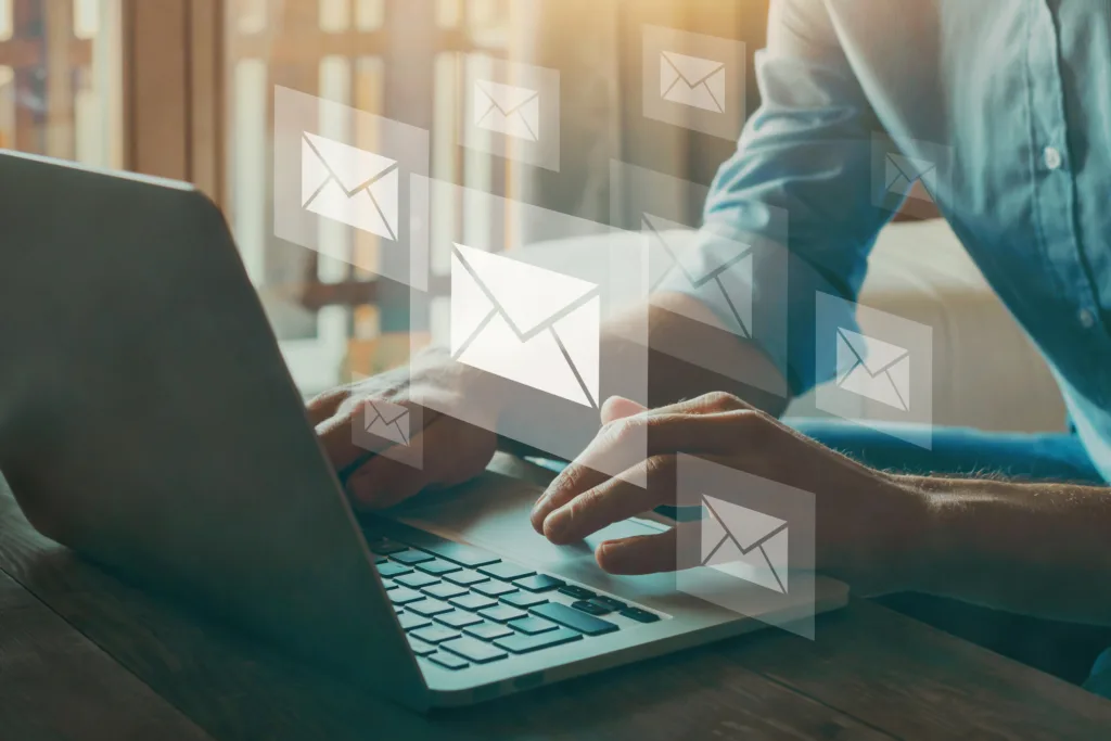 Hands rest on a laptop keyboard while 7 transparent boxes of varying sizes with envelope email icons on them float above the keyboard.