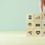 Pinched fingers hold a block with a heart and people in it, placing it on the top right corner of a stack of 3 by 3 blocks each representing an employee benefit.