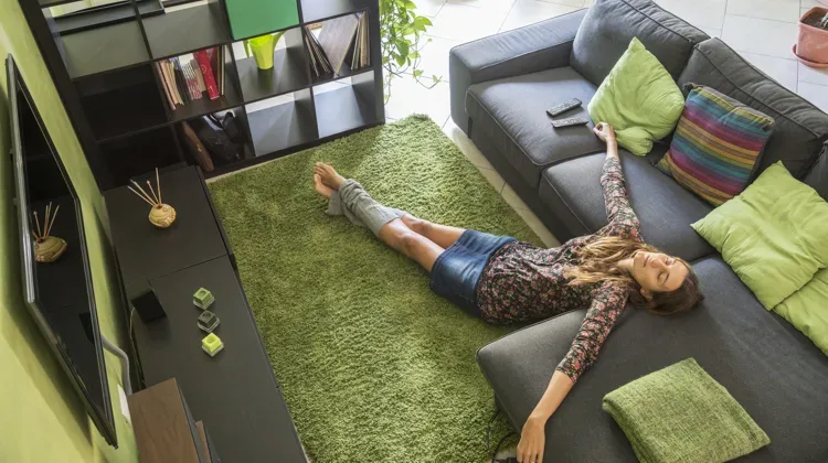 woman with her eyes closed lying on floor in front of a couch, arms akimbo with pillows strewn around her