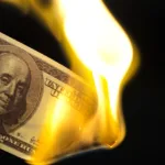 Close-up of a $100 bill with the corner on fire