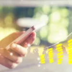 A hand holds a phone while a yellow bar graph with a line raising toward the right shows growth. There are certain industries that have a ton of opportunities for copywriters.